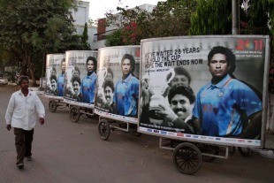 A man walks past a hoarding featuring Sachin Tendulkar and Kapil Dev in Ahmedabad, India, March 19, 2011