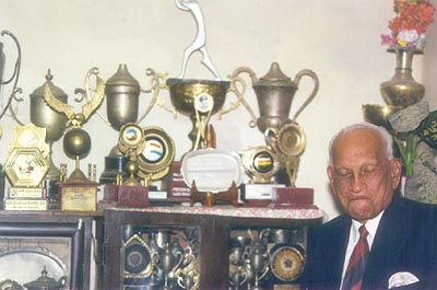 Mushtaq Ali in deep thought with his eyes closed as he sits in front of his numerous trophies